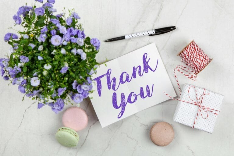 Thank You card with purple flowers, colorful macarons, gift box, and pen on a marble surface